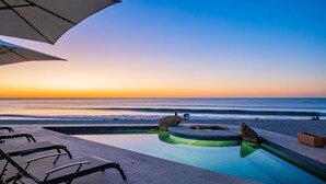 A poolside area with lounge chairs and a view of the ocean at sunset.