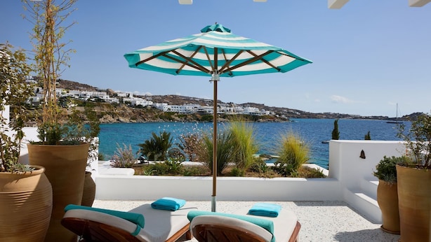 A terrace with two lounge chairs, a striped umbrella, and potted plants. - Nammos Hotel Mykonos (Mykonos)