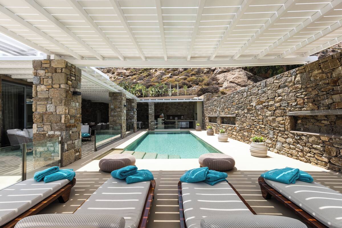 Un área junto a la piscina con sillas de descanso y una pared de piedra.