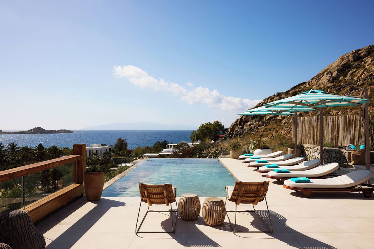 Zona junto a la piscina con sillones y sombrillas, con vistas a un cuerpo de agua.
