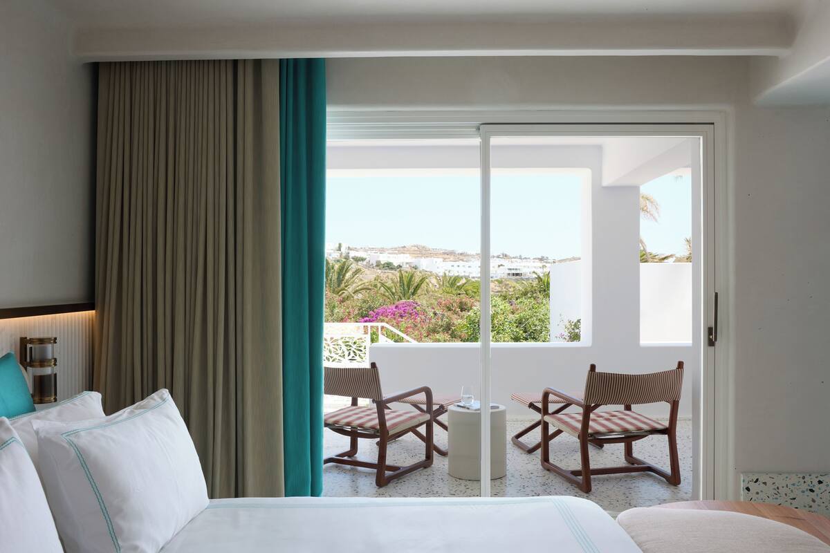 Habitación de hotel con una cama, un ventanal con vistas a la ciudad y dos sillas junto a la ventana.
