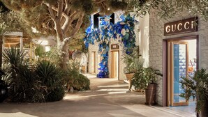 A pathway leading to a building with a 'GUCCI' sign, surrounded by lush greenery and large potted plants. - Nammos Hotel Mykonos (Mykonos)