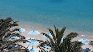 A beach with blue-striped umbrellas and lounge chairs, palm trees, and clear blue water. - Nammos Hotel Mykonos (Mykonos)