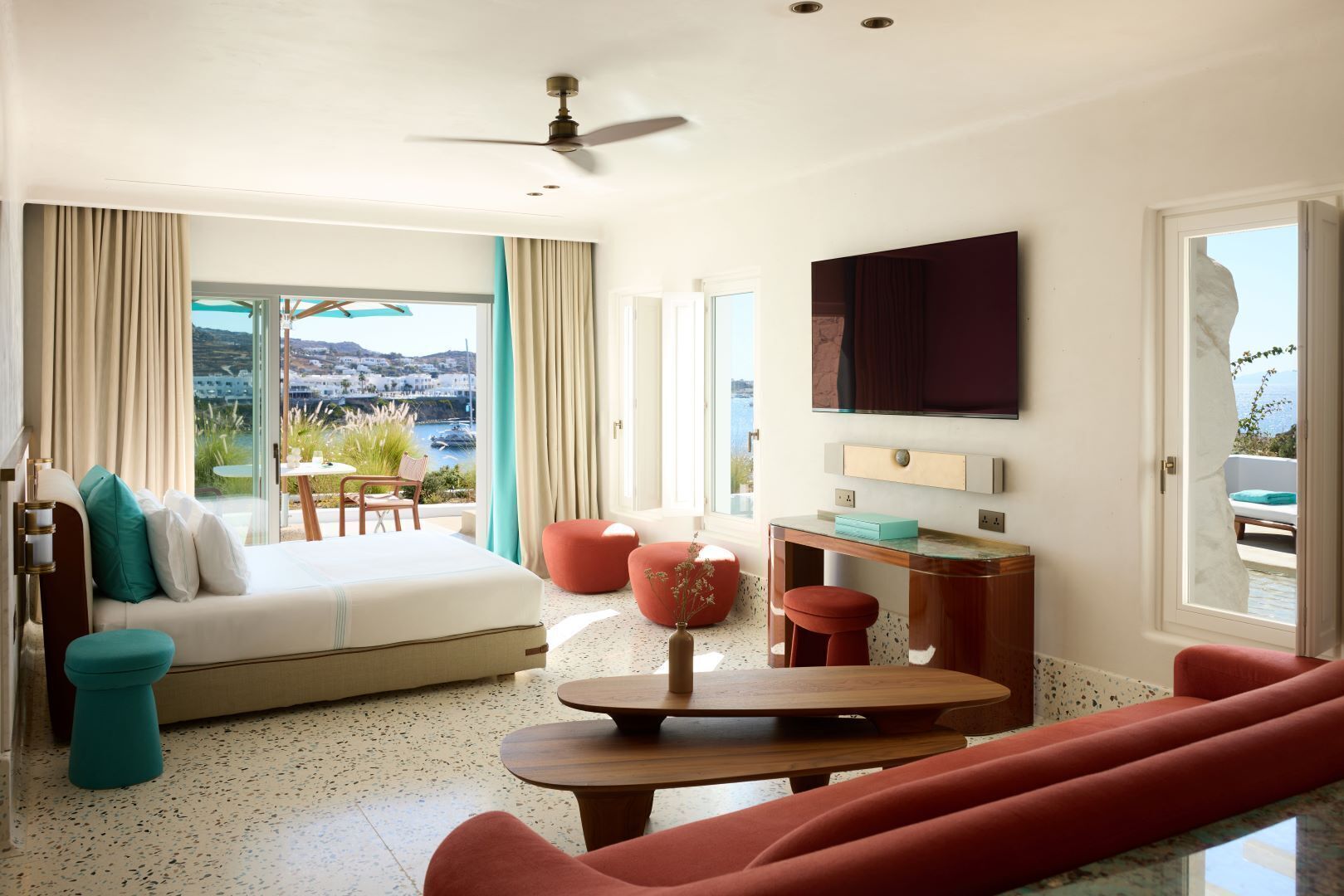 Ett hotellrum med en säng, ett skrivbord, en tv och utsikt över havet.