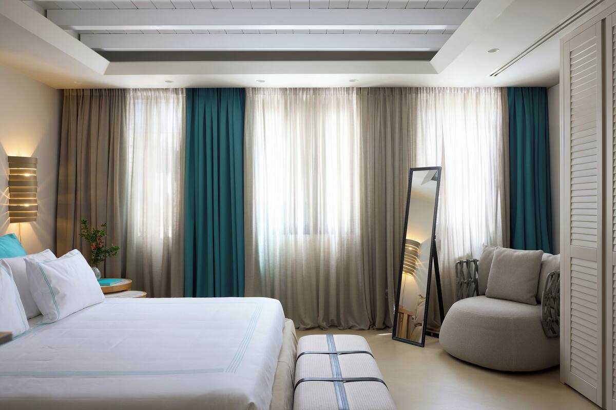 Una habitación de hotel con una cama grande, un área de descanso, un espejo y cortinas.