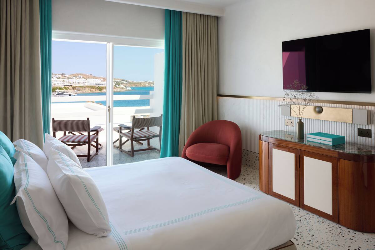 Habitación de hotel con cama, escritorio, silla, televisión y vista al mar.