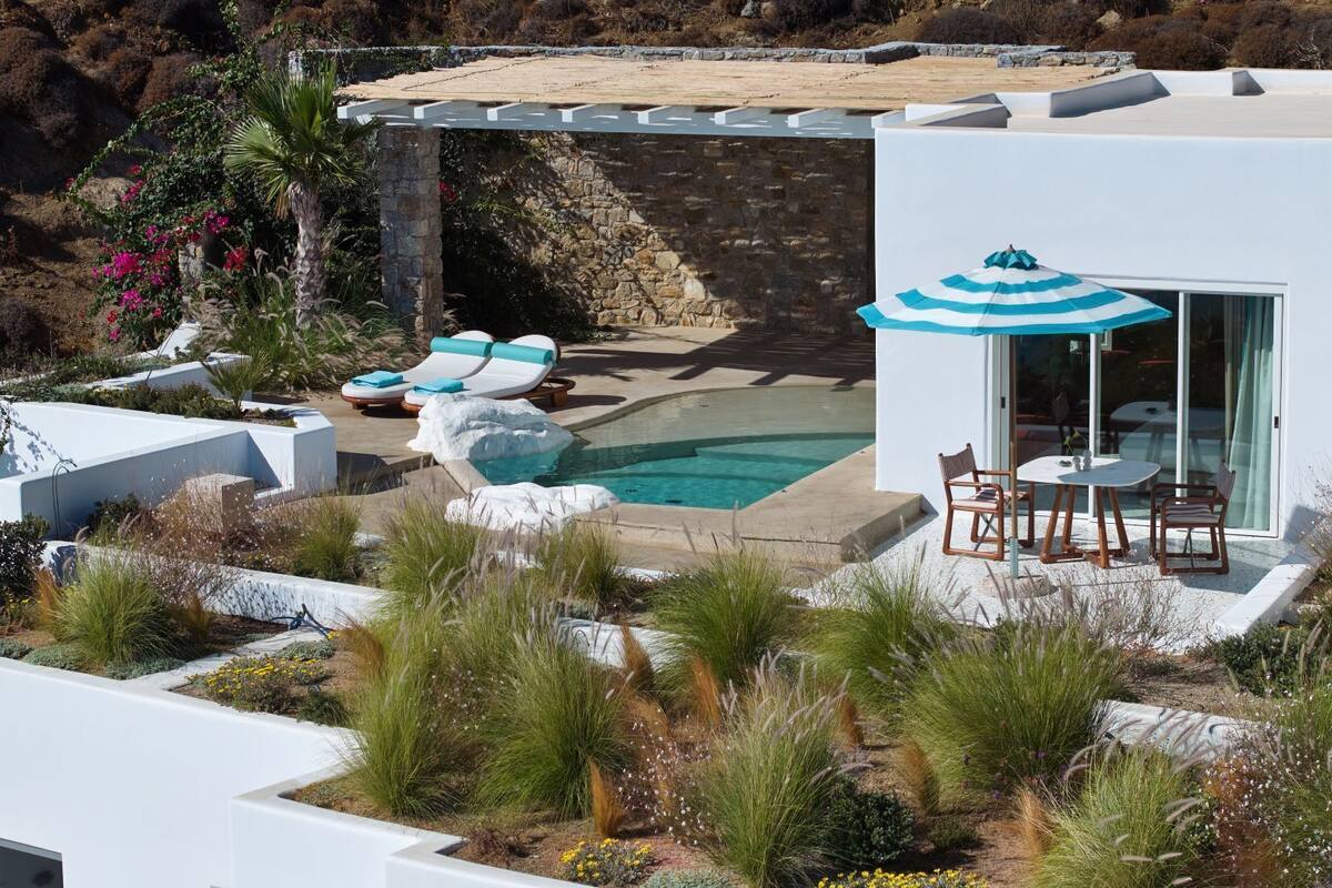 Un área de piscina moderna al aire libre con sillones de descanso, una mesa con sillas y una zona de estar cubierta con sombrilla.