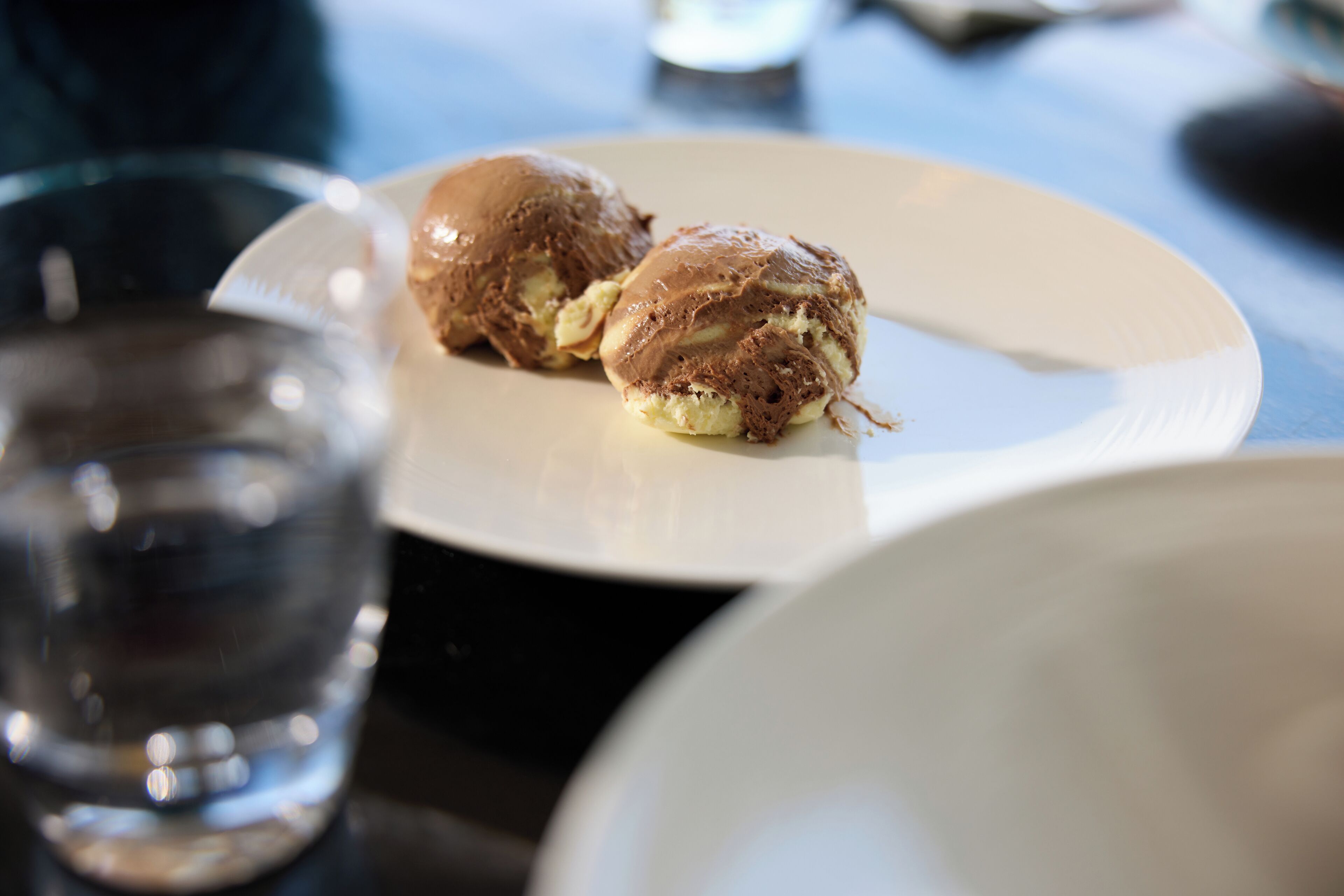 Two pastries on a white plate, a glass of water, and a blurred background.
