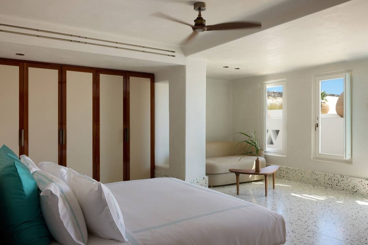 Un dormitorio con una cama, un armario de madera, una mesita con una planta y vistas al exterior a través de una ventana.