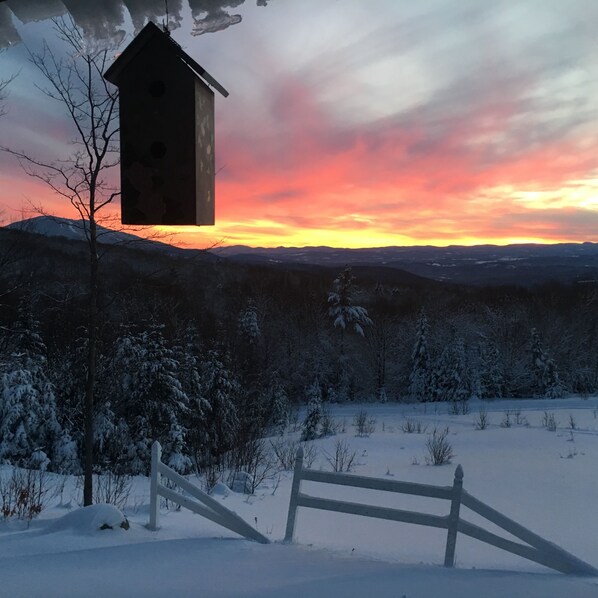 A wooden birdhouse on a snowy hill with a sunset in the background.