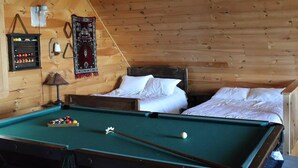 Una habitación acogedora con mesa de billar, dos camas, paredes de madera, una lámpara y un tapiz decorativo.