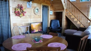 Interior acogedor de una cabaña con una mesa de comedor de madera, sillas, un televisor, una chimenea y una escalera.