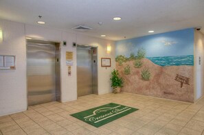 An elevator area with a beach mural, a green mat with 'Crescent Shores' text, and a sign reading 'SOUTH TOWER'.