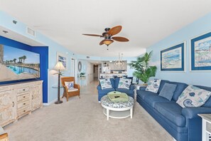 Un salon avec un canapé bleu, une table basse, un fauteuil en osier et un ventilateur de plafond.
