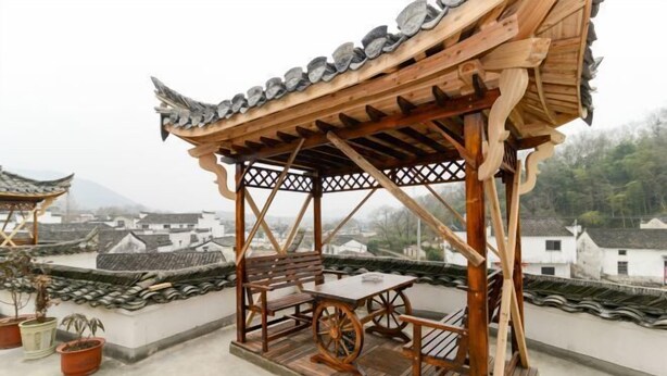 A traditional wooden pavilion with a table and benches on a rooftop, surrounded by terracotta pots and traditional roof tiles. - Huiyun Inn (Jing County)