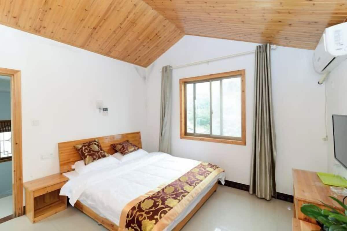 Quarto com teto de madeira, cama com colcha estampada, janela com cortinas e televisão na parede.