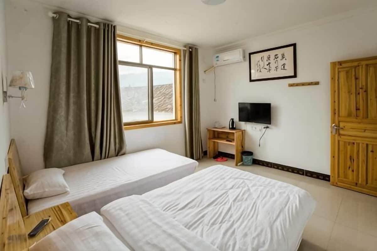 Quarto com duas camas, televisão, escrivaninha de madeira e janela com cortinas.
