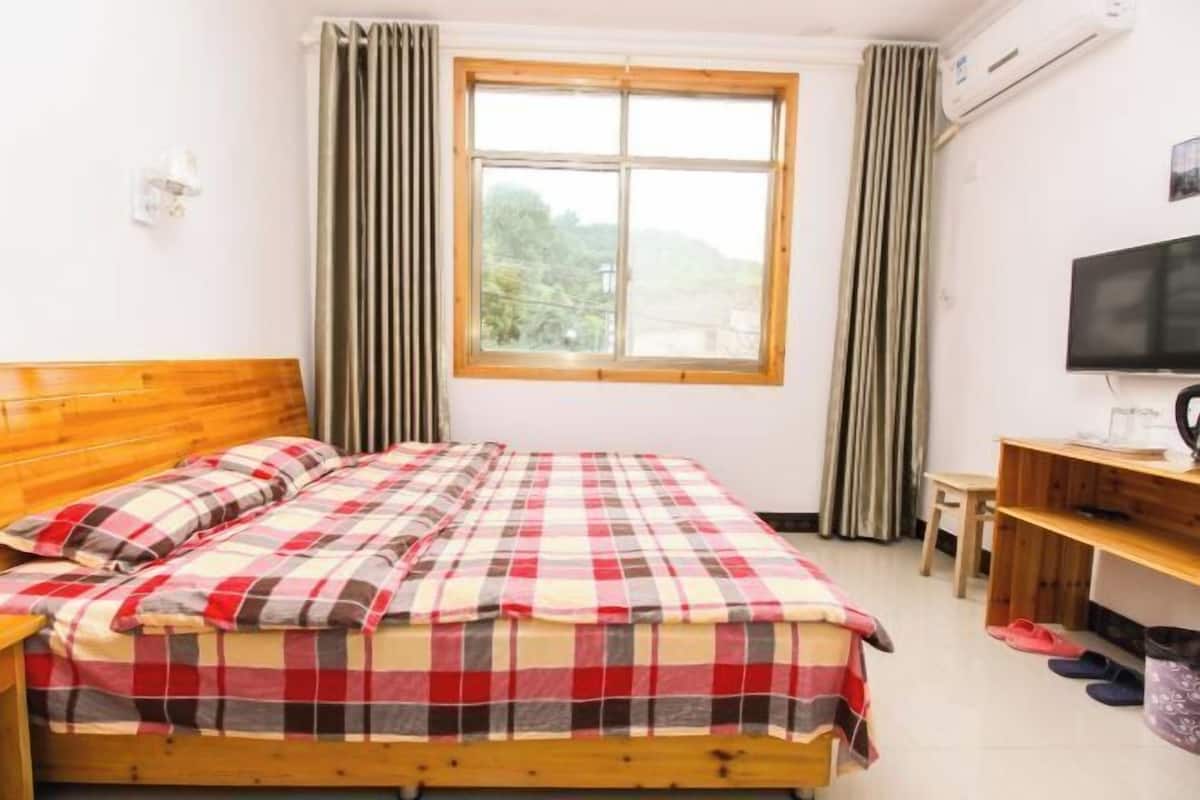 Quarto com cama de madeira, janela com cortinas, televisão e escrivaninha com cadeira.