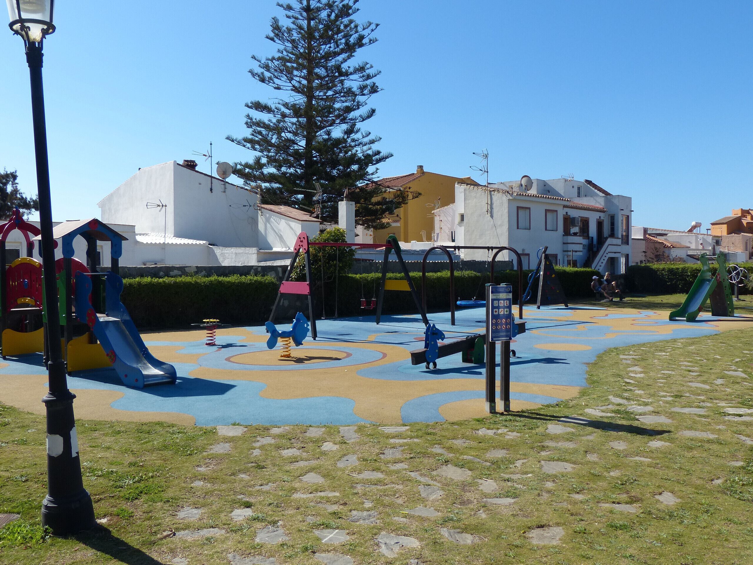 Parque infantil com diversos equipamentos de lazer, incluindo escorregadores e balanços, cercado por uma área pavimentada com design padronizado.