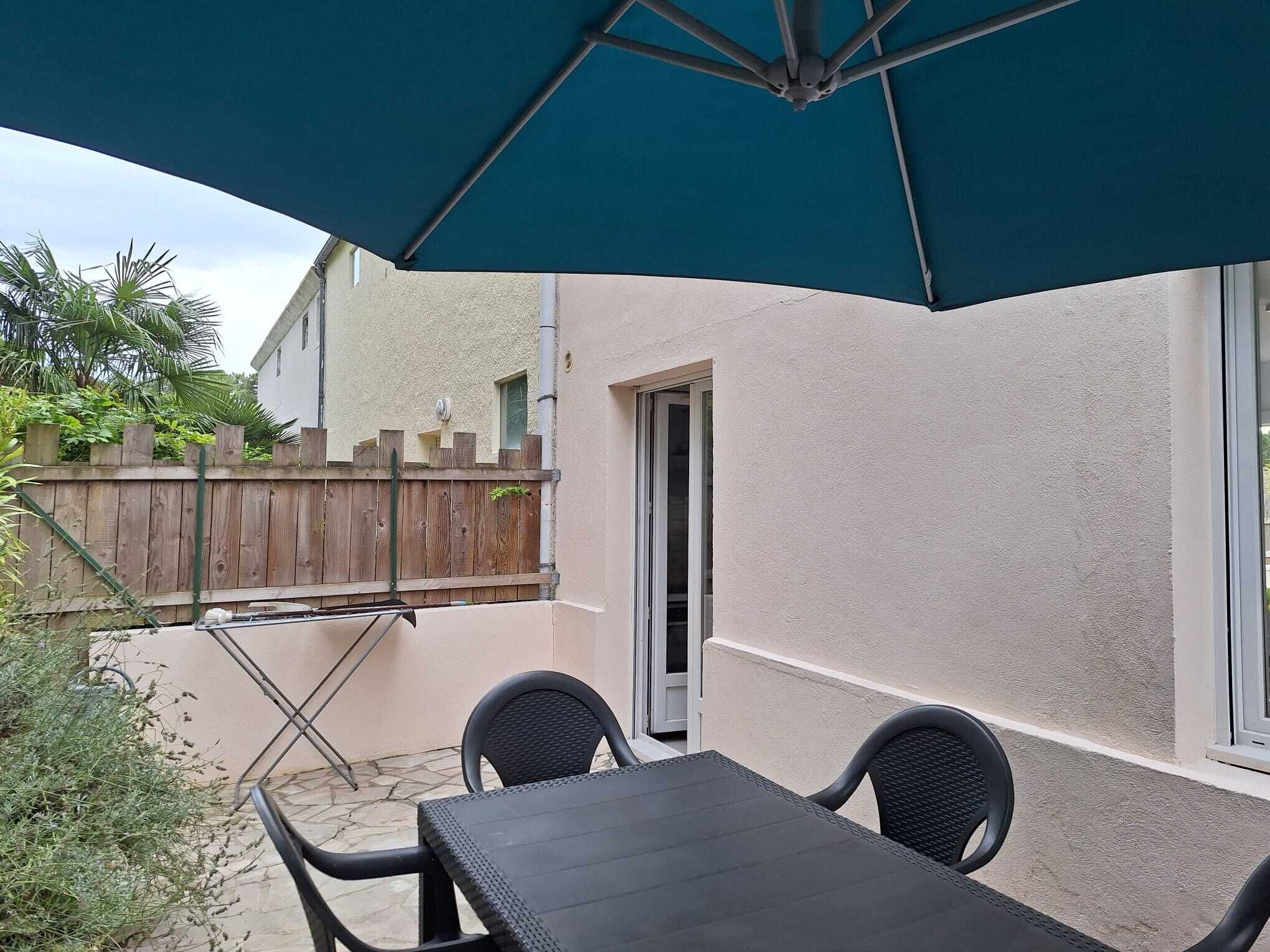 A patio with a table and chairs, a wooden fence, and a building with a door and windows.