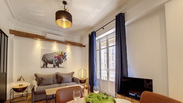En stue med en sofa, et spisebord med tallerkener og en salatskål, et fjernsyn og et vindue med gardiner.