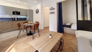 Et moderne køkken med indbyggede apparater, et spiseområde med et træbord og stole, og en hyggelig opholdsstue med en seng og et stort vindue.