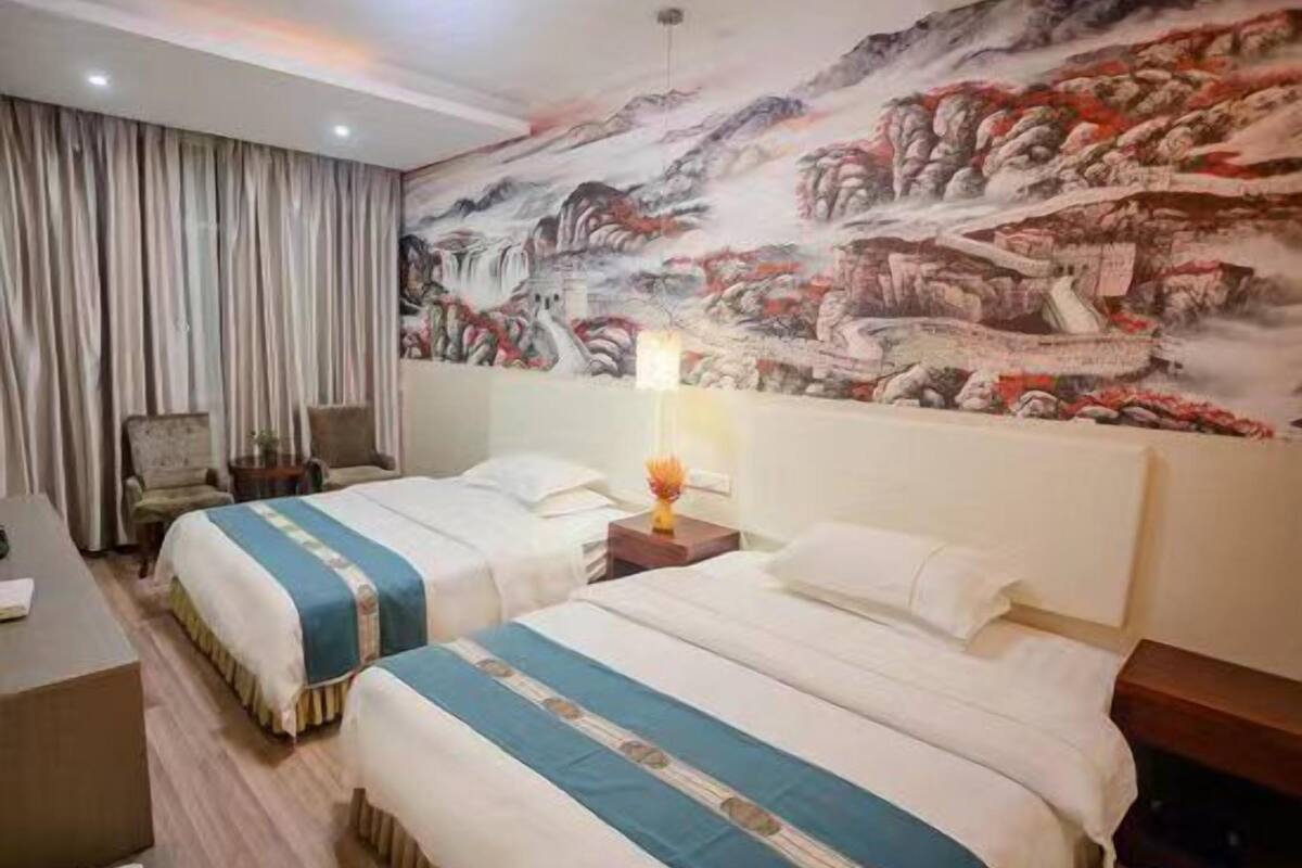 Habitación de hotel con dos camas, un mural grande en la pared, un escritorio y una silla.