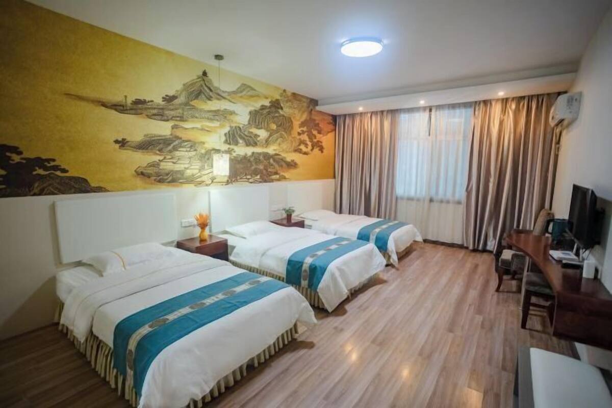 Habitación de hotel con dos camas, un mural grande, un televisor y un escritorio.