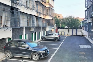 Un estacionamiento con dos coches, un edificio con balcones y un árbol.