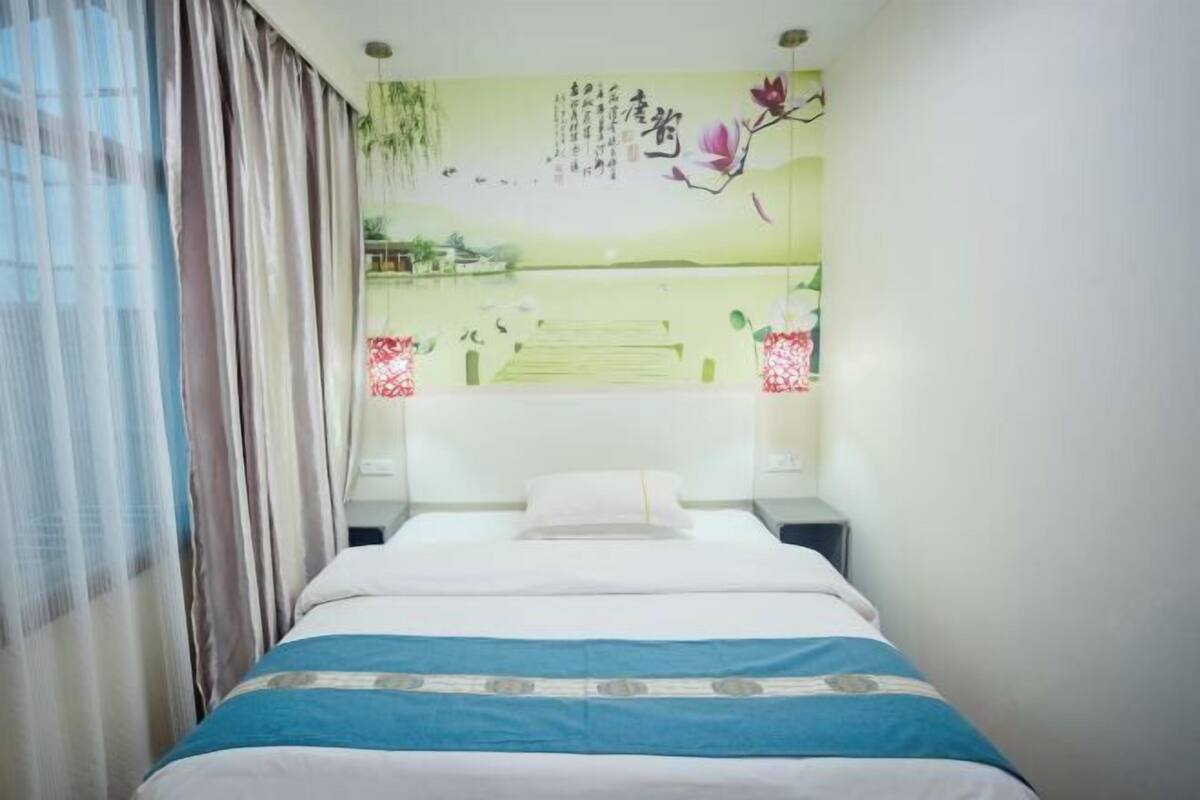 Un dormitorio con cama, cortinas, una pared con obras de arte y una mesita de noche.