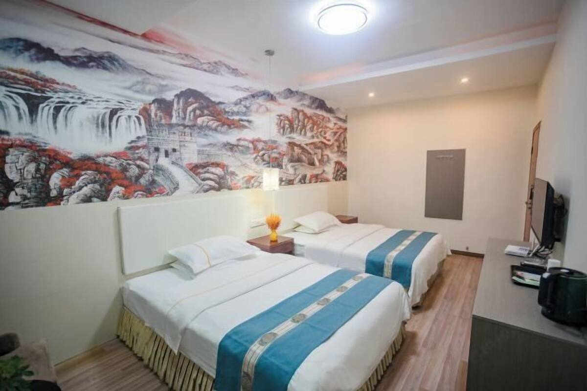 Habitación de hotel con dos camas, un mural en la pared, un escritorio y un televisor.