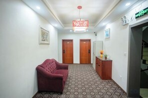 A hallway with a patterned carpet, a red sofa, two wooden doors, a reception desk, and a hanging light fixture. - Hengyang Wangyuelou Homestay (Mount Heng Scenic Area Nanyue Grand Temple) (Hengyang)