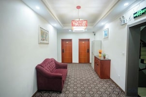 A hallway with a patterned carpet, a red sofa, two wooden doors, a reception desk, and a hanging light fixture.