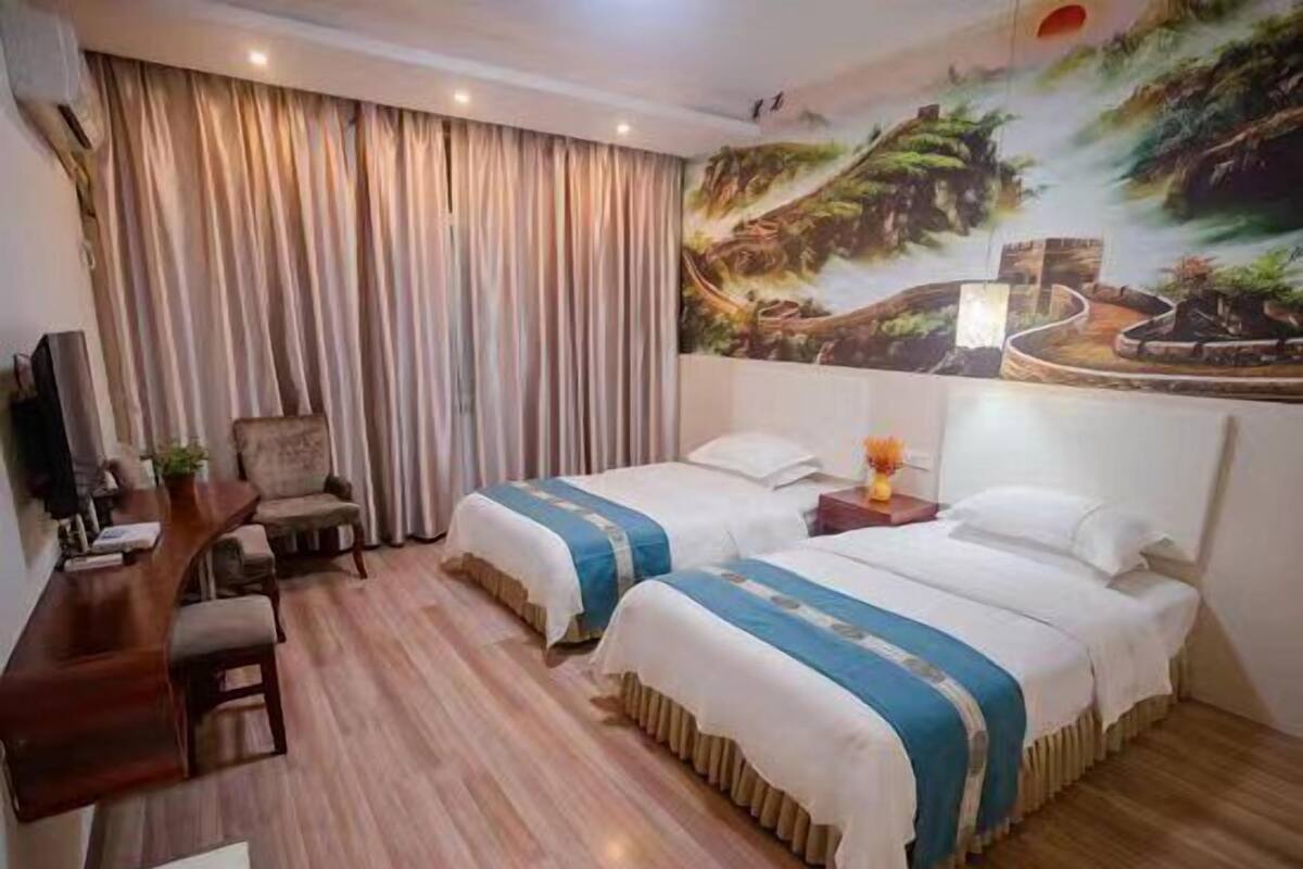 Habitación de hotel con dos camas, un escritorio, una silla y un mural grande en la pared.