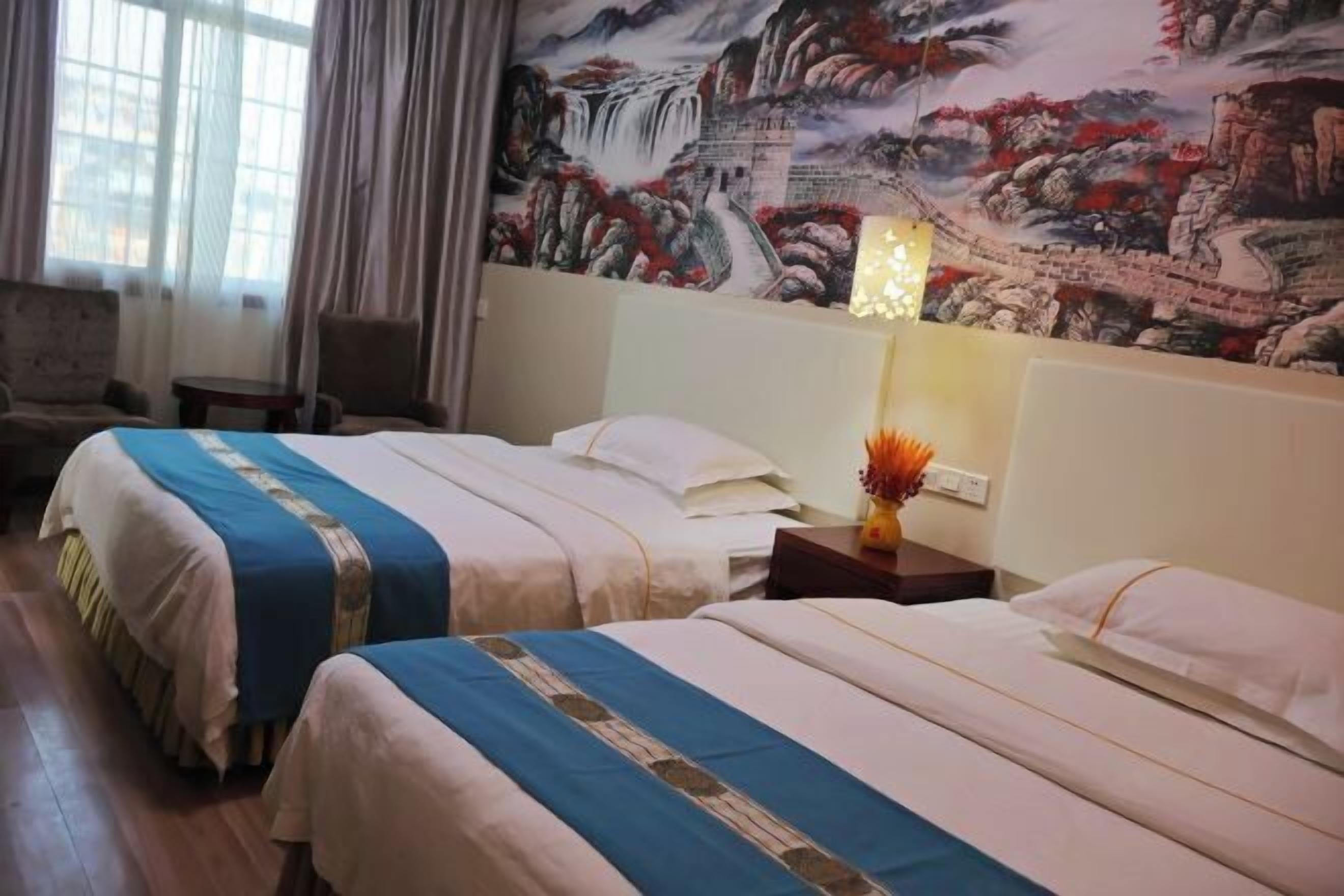 Habitación de hotel con dos camas, un mural en la pared, una mesita de noche con lámpara y vistas al exterior por la ventana.