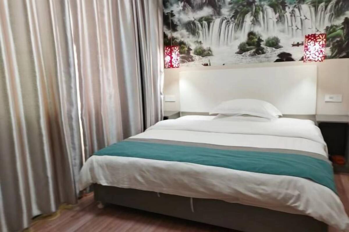 Una cama bien hecha con colcha blanca y aguamarina, cabecera con un mural de cascada y dos luces decorativas rojas a cada lado.
