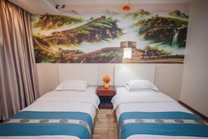 Habitación de hotel con dos camas, un mural de un paisaje en la pared y una mesita de noche con un jarrón de flores.