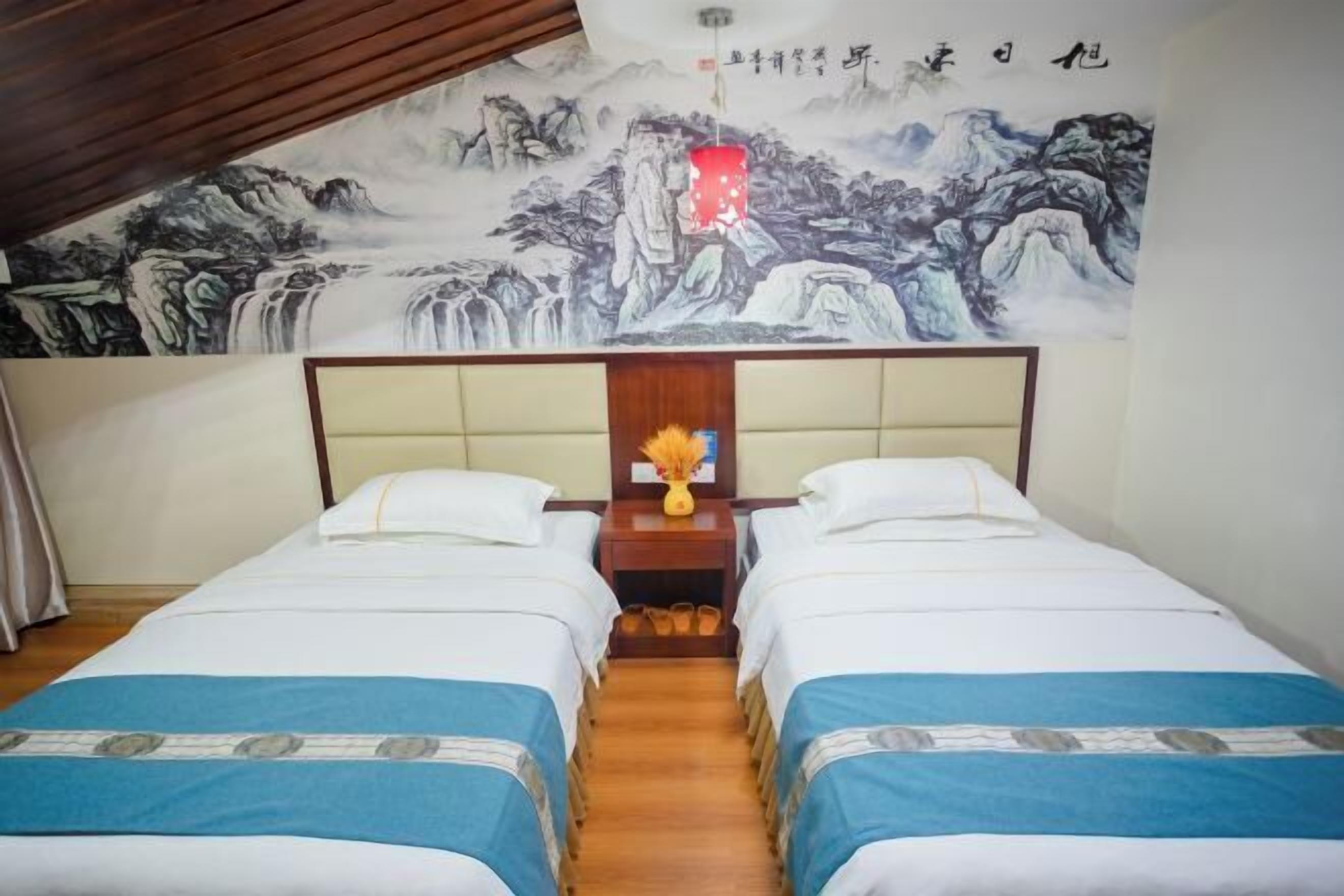A room with two beds, a wooden headboard, a mural on the wall, and a small table with a vase.