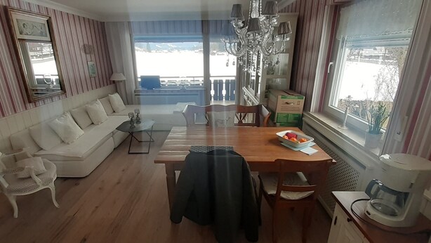 Una habitación con mesa de comedor, sillas, un sofá, una araña y vistas al exterior.
