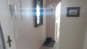 Un pasillo con suelo de madera, una puerta a la izquierda, un espejo en la pared y una cesta a la derecha.