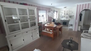 Un comedor con una mesa y sillas de madera, un mueble blanco con puertas de vidrio y una cocina al fondo.