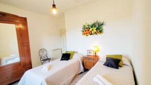 Een slaapkamer met twee bedden, een houten garderobe, een spiegel, een radiator en een bloemenarrangement aan de muur.