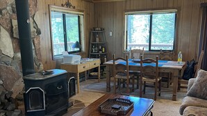 L’intérieur chaleureux d’un chalet avec un mur en pierre, un poêle à bois, une table à manger avec des chaises et un coin salon confortable comprenant un canapé et un fauteuil.