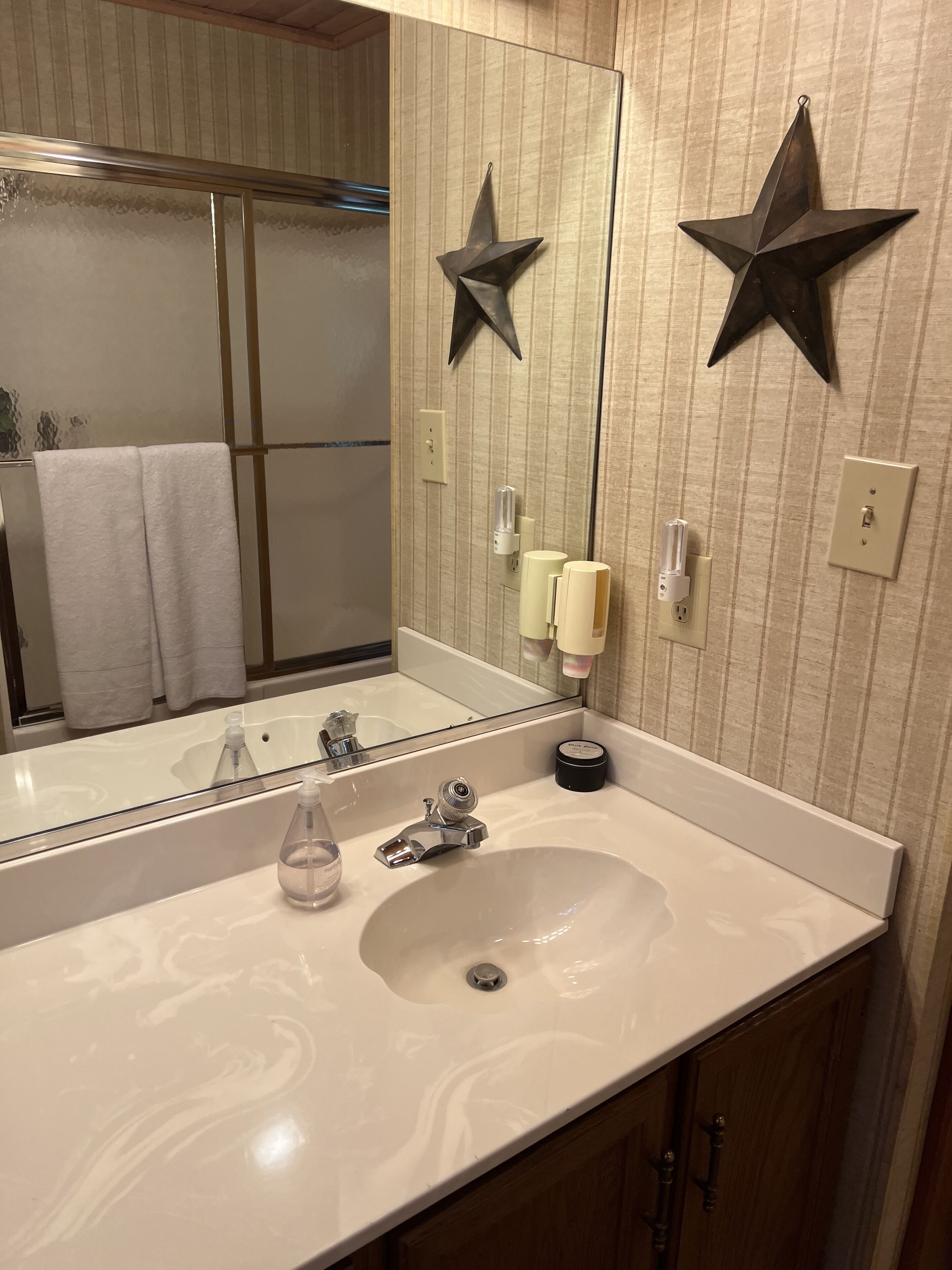 A bathroom with a large mirror, a white sink, and two star-shaped wall decorations.