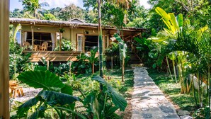 A tropical garden with a stone pathway leading to a wooden house with a thatched roof. - Villas Sampaguita (El Nido)