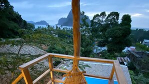 A wooden deck with a hanging basket, a pool, and a view of mountains and trees. - Villas Sampaguita (El Nido)