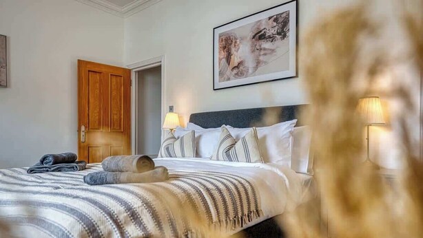 Een hotelkamer met een bed, een houten deur, een kunstwerk in een lijst aan de muur en een lamp.