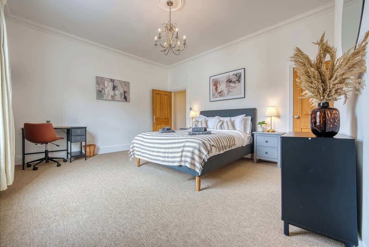 A bedroom with a bed, desk, chair, and a dresser.