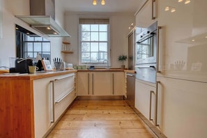 A kitchen with wooden flooring, white cabinets, a window, and a built-in oven.