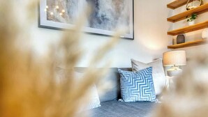 Een slaapkamer met een bed, kussens, een wandlamp en een plank met spullen.